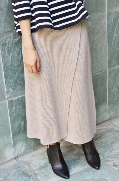 ベージュのラップ風ニットスカートと黒いブーツを履いた女性