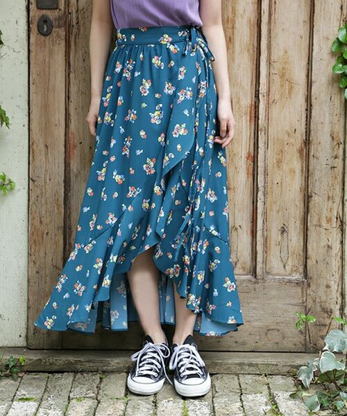 ブルーの花柄スカートに黒いスニーカーを履いた女性の脚