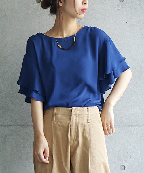 ネイビーのフリルトップスにベージュのパンツを履いた女性