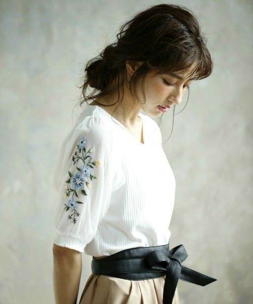 白い花柄刺繍のトップスにベージュのボトムスを履きサッシュベルトをした女性
