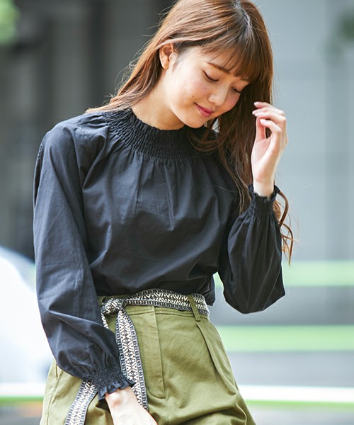 黒い長袖ブラウスにカーキパンツを履いた女性