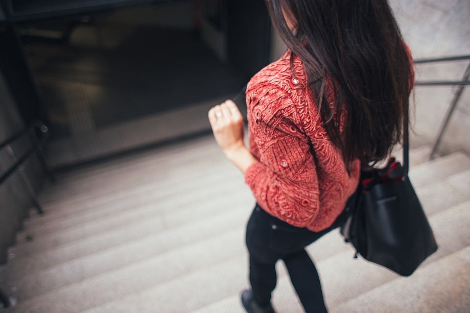 赤のニットセーターと黒のレザーショルダーバッグを持った女性