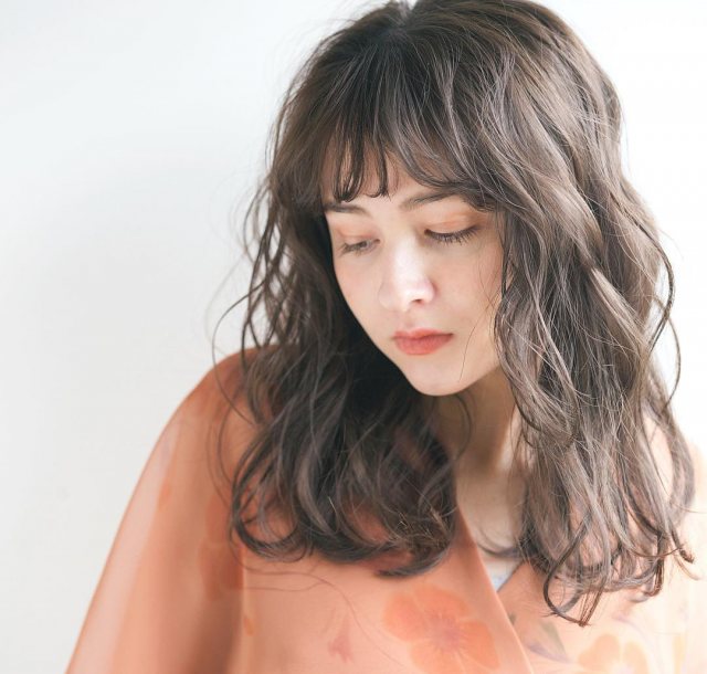 丸顔さんに似合う髪型の前髪ありのナチュラルなパーマミディアムヘアスタイルにした女性の画像