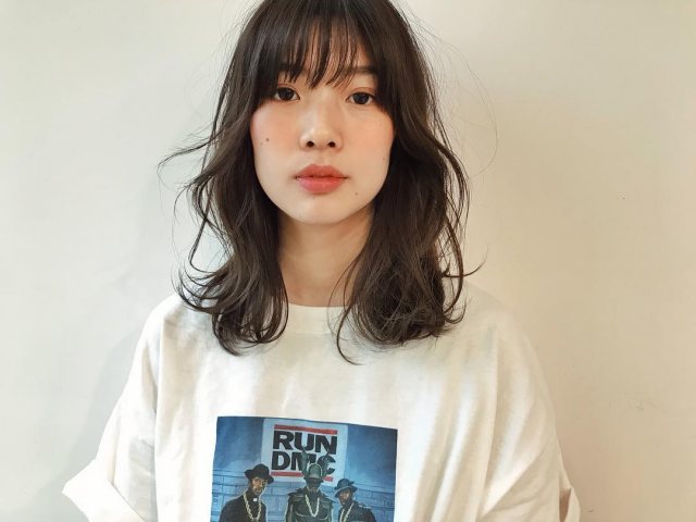丸顔さんに似合う髪型の前髪ありの黒髪くせ毛風パーマミディアムヘアスタイルにした女性の画像