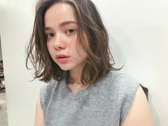 丸顔さんに似合う髪型の前髪なしのパーマミディアムヘアスタイルにした女性の画像