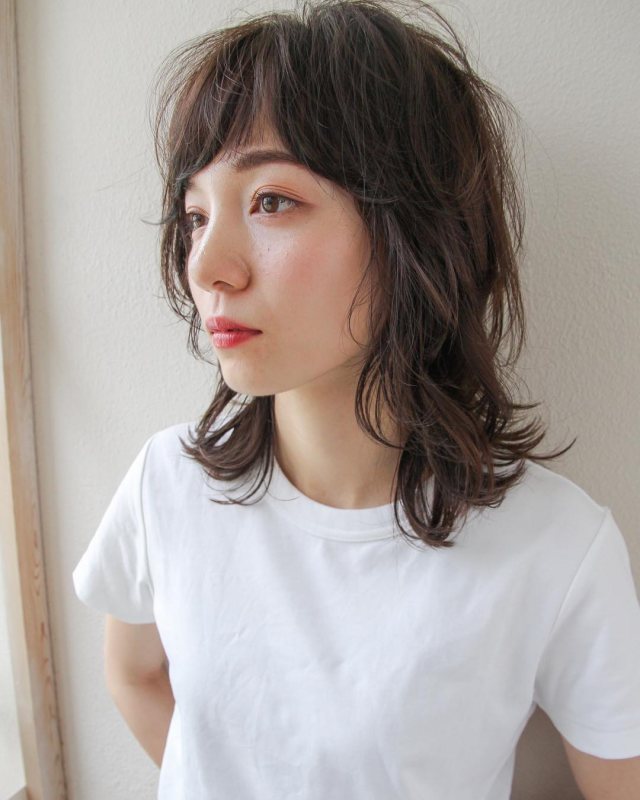 丸顔さんに似合う髪型の前髪ありのウルフパーマミディアムヘアスタイルにした女性の画像