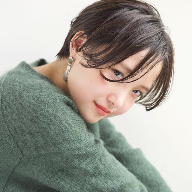 丸顔さんに似合う髪型の前髪なしの黒髪ショートヘアスタイルにした女性がグリーンニットを着た画像