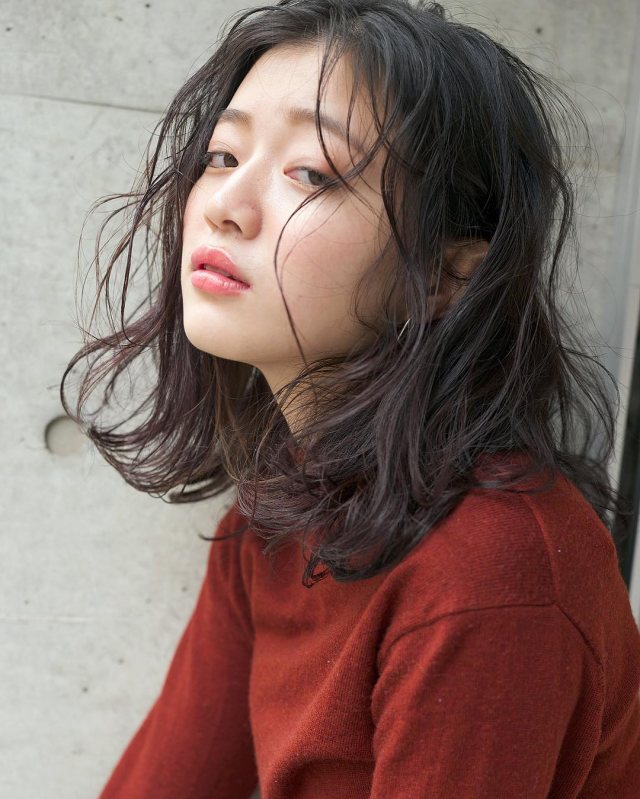 丸顔さんに似合う髪型の前髪なしの黒髪パーマミディアムヘアスタイルにした女性の画像