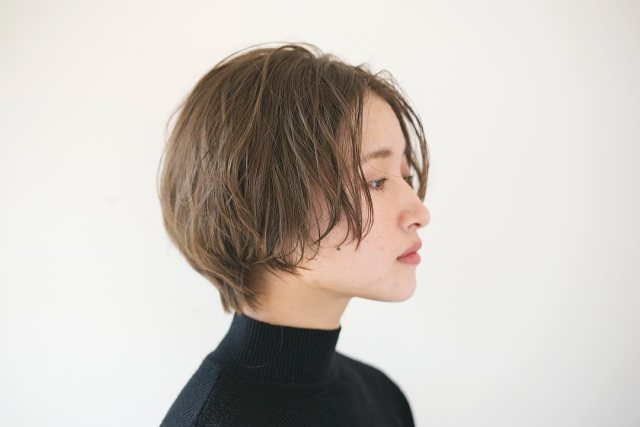 丸顔さんに似合う髪型の前髪なしのブラウンパーマショートヘアスタイルにした女性が黒タートルニットをきた画像