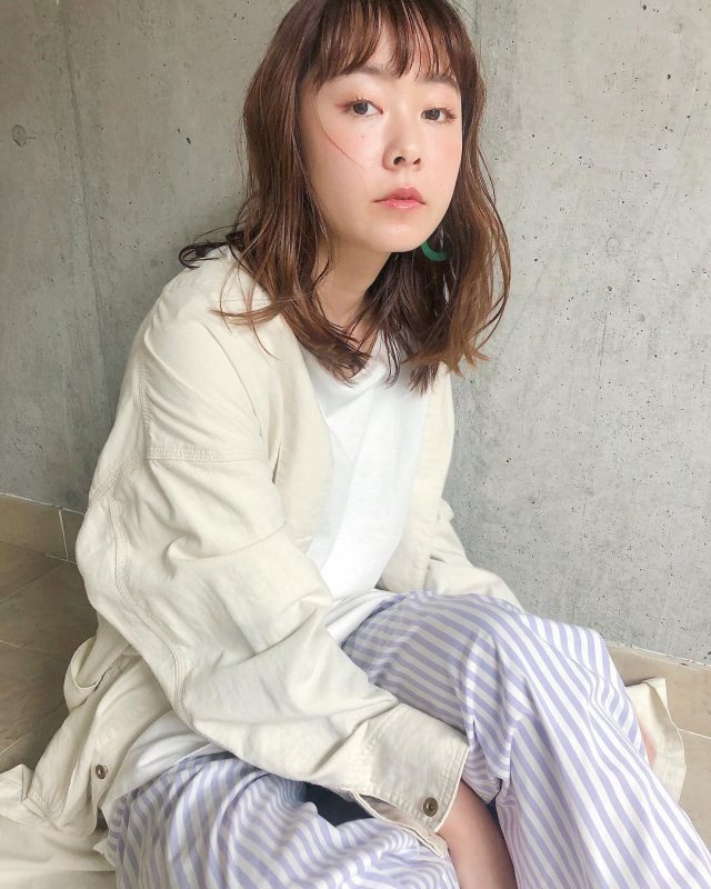 丸顔女子に似合う髪型の前髪ありのニュアンスパーマミディアムヘアスタイルにした女性の画像