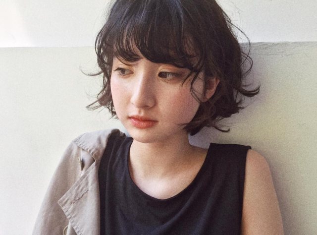 丸顔さんに似合う髪型の前髪ありの黒髪パーマショートボブヘアスタイルにした女性の画像