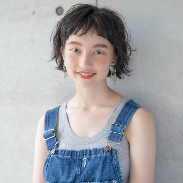 丸顔さんに似合う髪型の前髪ありの黒髪パーマボブヘアスタイルにした女性の画像