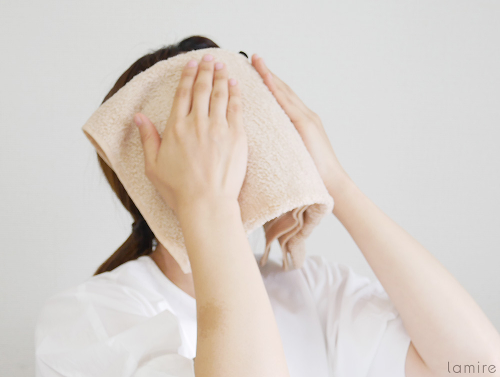 蒸しタオルを顔にあてている女性の写真