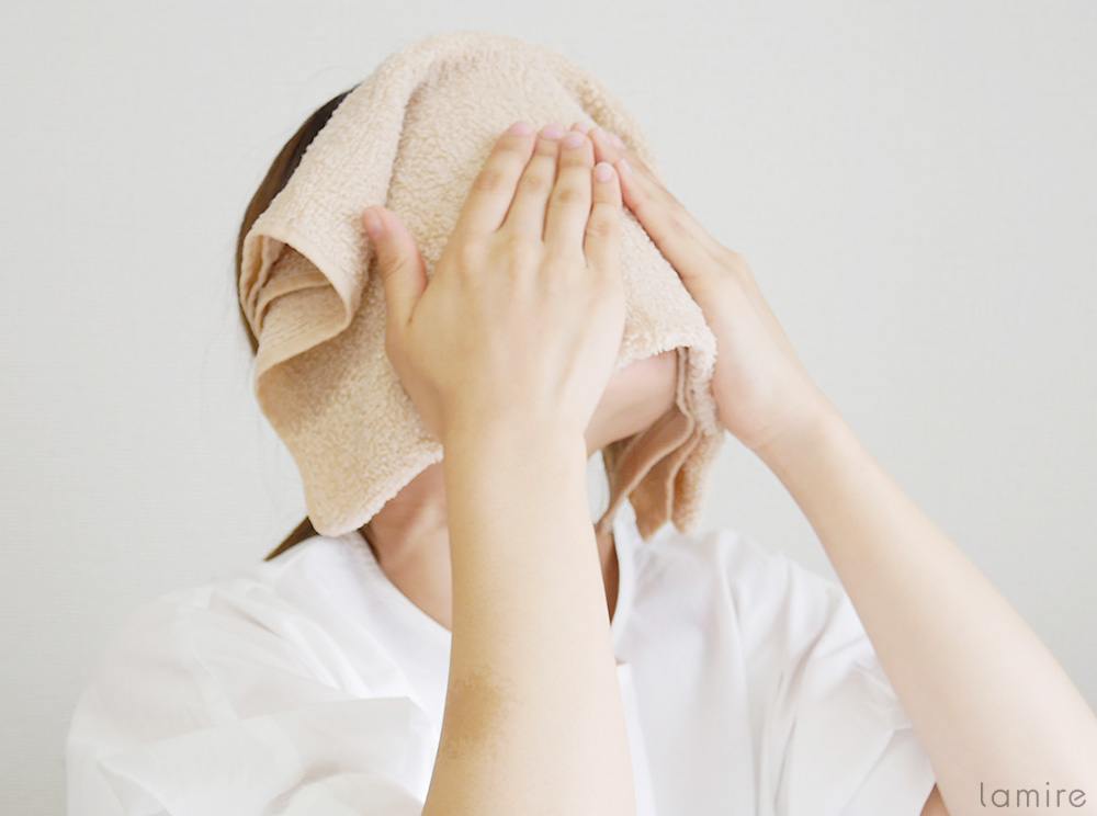 蒸しタオルを顔にあて、手で押さえている女性の写真