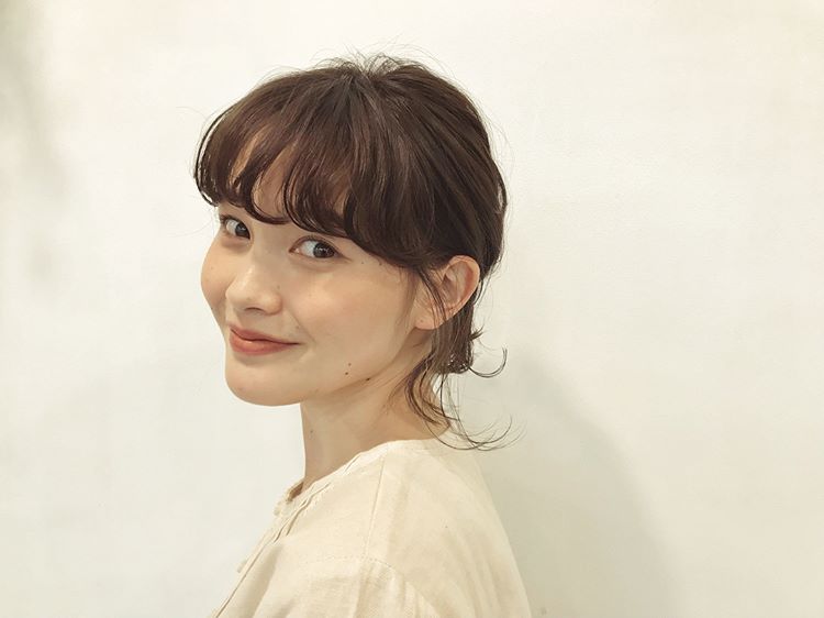 前髪ありのミディアムヘアスタイルを後れ毛を出したまとめ髪にヘアアレンジにしている女性