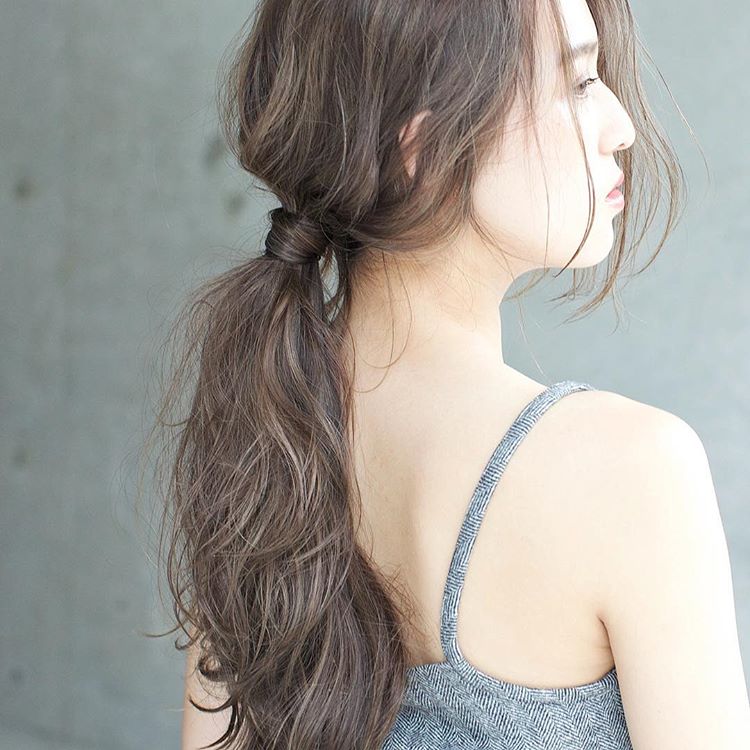 前髪なしのロングヘアスタイルを後れ毛を出したローポニーテールヘアアレンジにしている女性