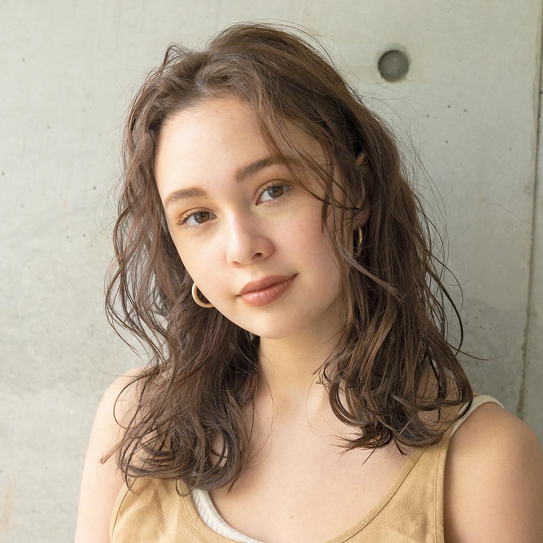 丸顔な輪郭でも小顔に見える前髪の前髪なしのパーマロングヘアスタイルにした女性の画像