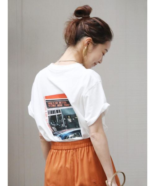 白のバックフォトTシャツとオレンジのボトムスを合わせる女性