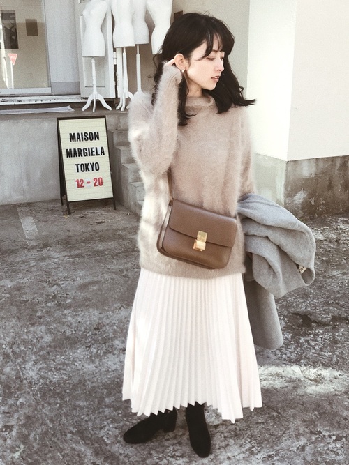 ベージュアンゴラファー調ニットに白プリーツスカートを履いた女性
