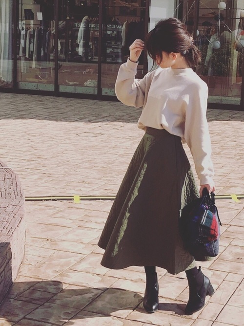 ベージュワイド袖スウェットにカーキキルトフレアスカートを履いた女性