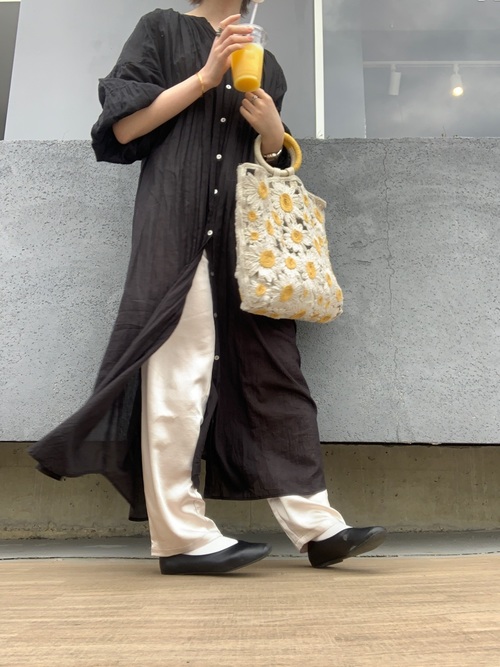 黒いシャツワンピースに白いパンツ、花柄のニットバッグを持ったコーデ