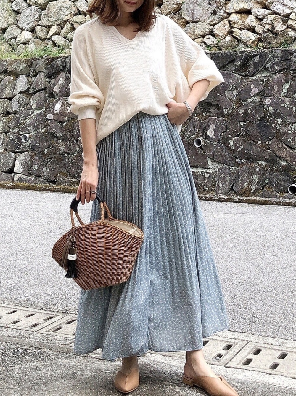 白のVネックトップスにブルーのプリーツスカートを履いた女性