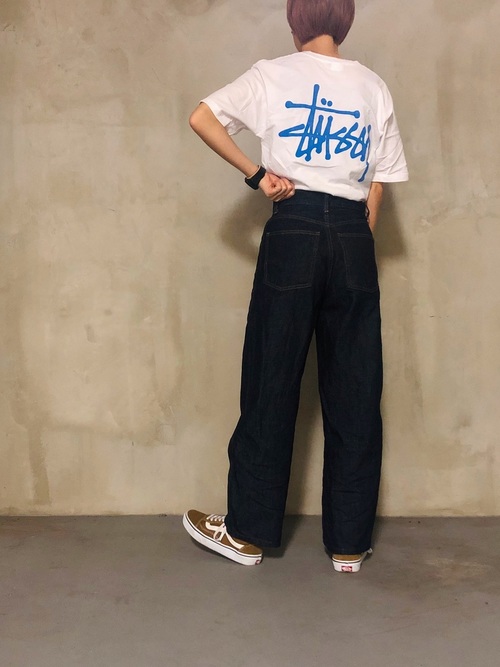 白バックロゴSTUSSY Tシャツとデニムカーブパンツにブラウンスニーカーを履いた女性