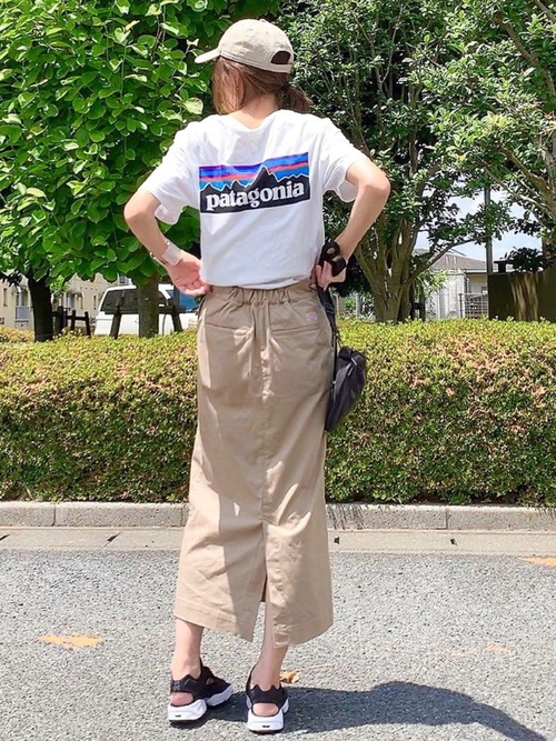 パタゴニアの半袖白Tシャツとベージュタイトスカートに黒スポーツサンダルを履いた女性