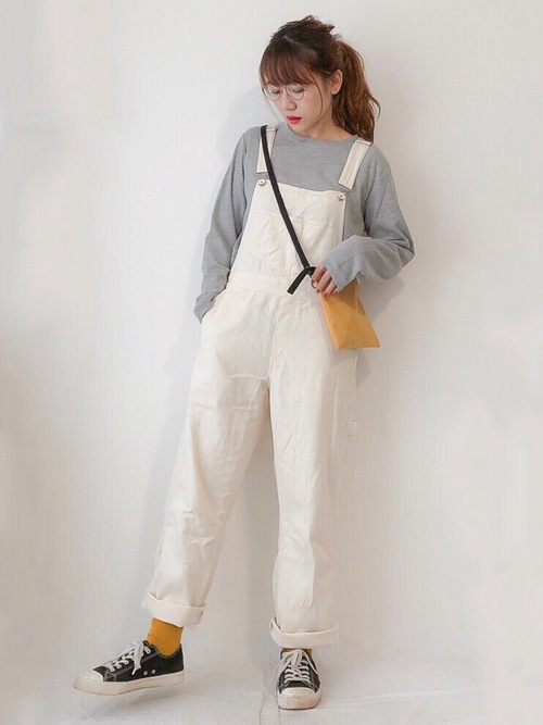 マスタードサコッシュとグレーロングTシャツに白デニムサロペットを履いた女性