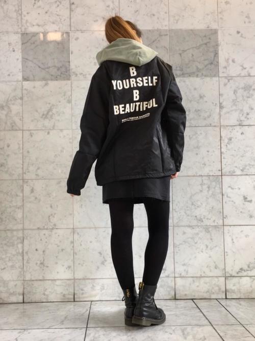 黒コーチジャケットとグリーンパーカーに黒デニムミニスカートを履いた女性