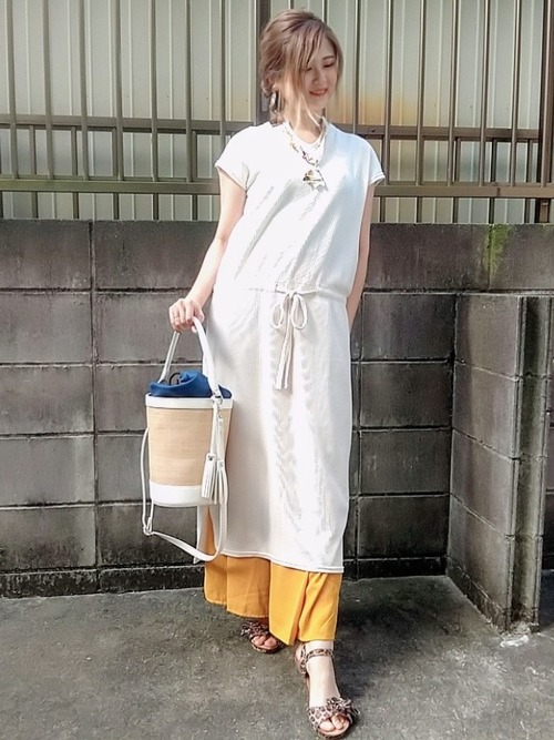 白ロングワンピースとイエローフレアパンツに巾着かごバッグを合わせた女性