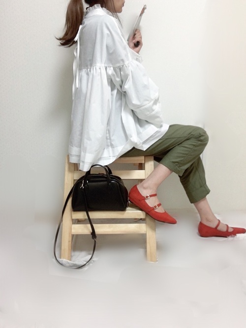 白ハイネックフレアブラウスとカーキパンツにオレンジダブルストラップパンプスを履いた女性