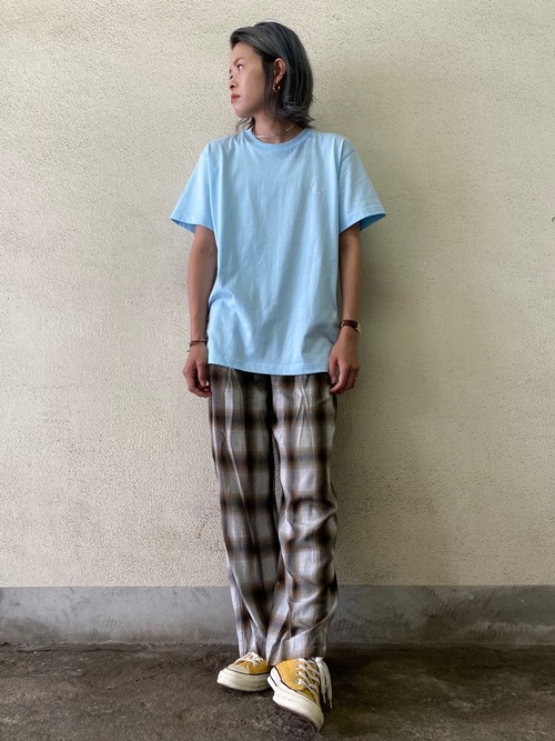 水色クルーネックオーバーサイズTシャツとブラウンチェックストレートパンツにコンバースのサンフラワーチャックテイラーを履いた女性