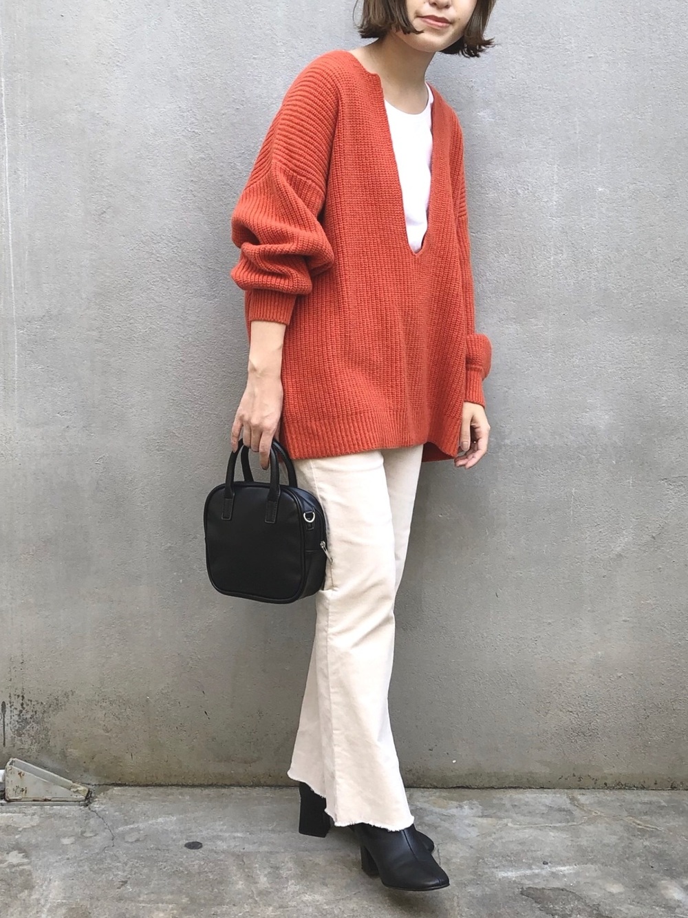 オレンジのニットに白のパンツのコーデ