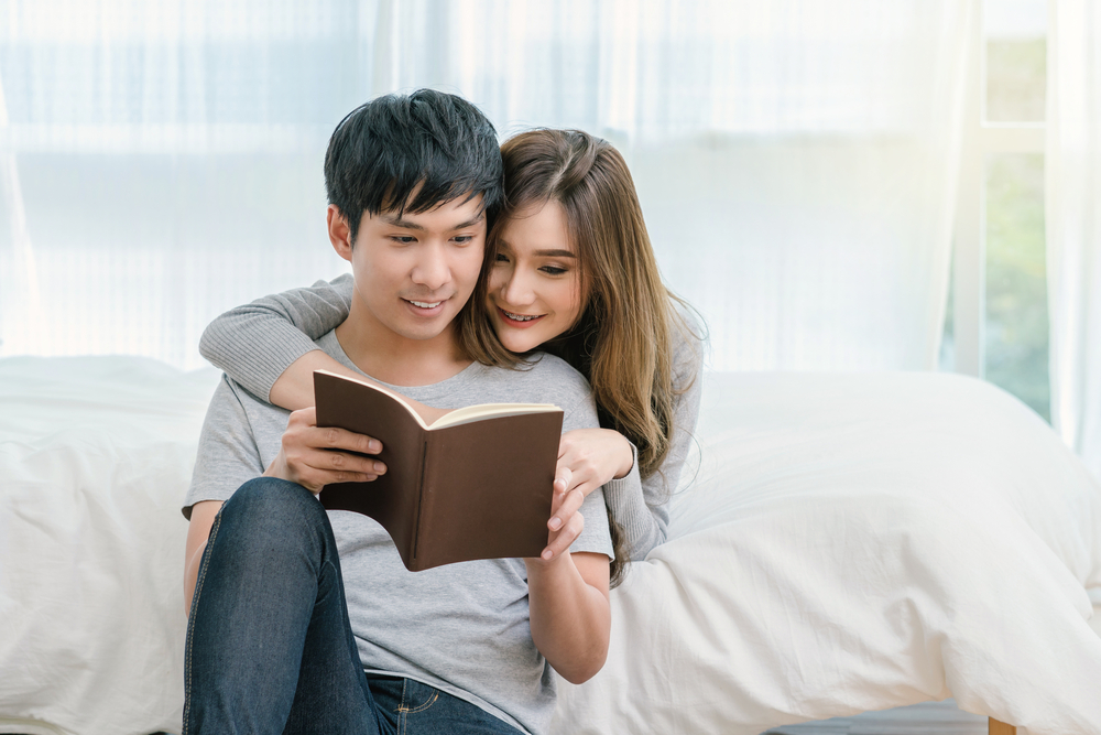 男性の後ろから一緒に本を見る女性