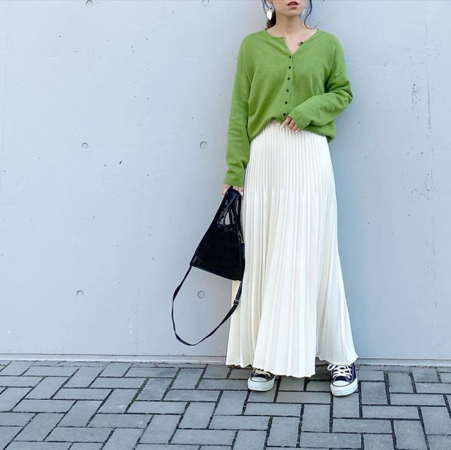 緑のカーディガンに白のプリーツスカートを着た女性