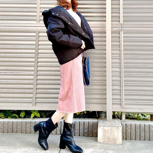 黒ダウンジャケットと白ニットにピンクコーデュロイスカートを履いた女性