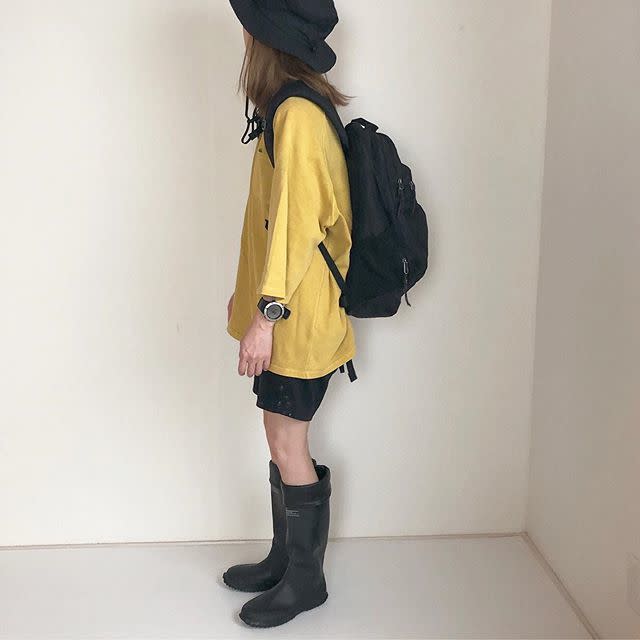 黒のバケットハットに黄色のビックTシャツと黒のショートパンツと黒のロングブーツを合わせたコーディネート