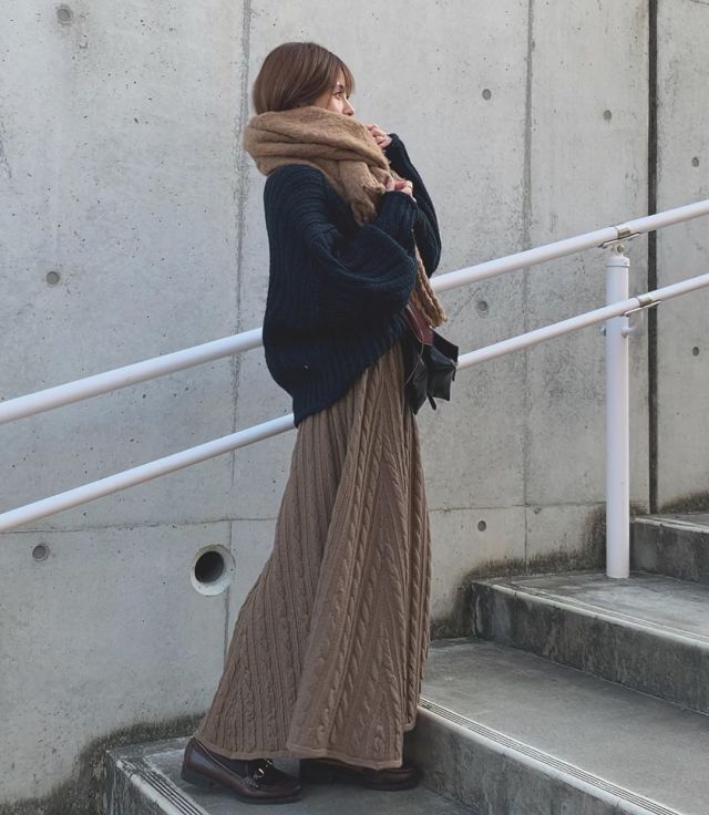 黒いチャンキーニットにケーブルニットスカートを着ている女性の写真