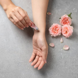 手にバラの香りの香水をつける女性
